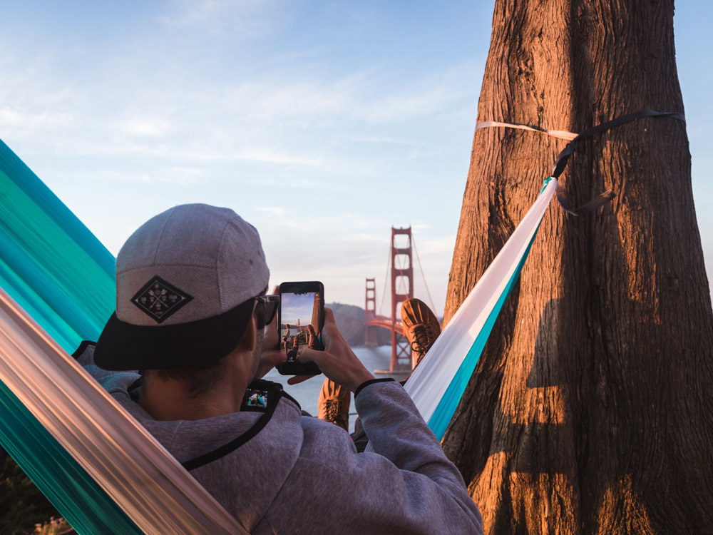 a man taking a picture on his mobile phone while sitting on a hammock